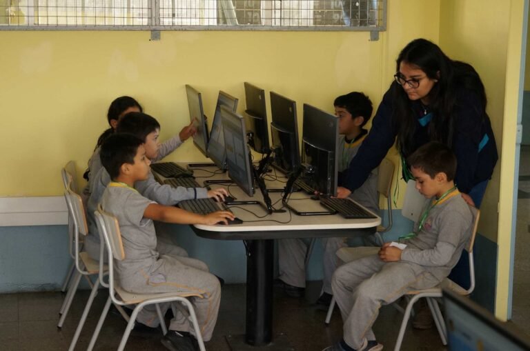 Estudiantes de Educación Básica trabajan en computadores acompañados por su profesora