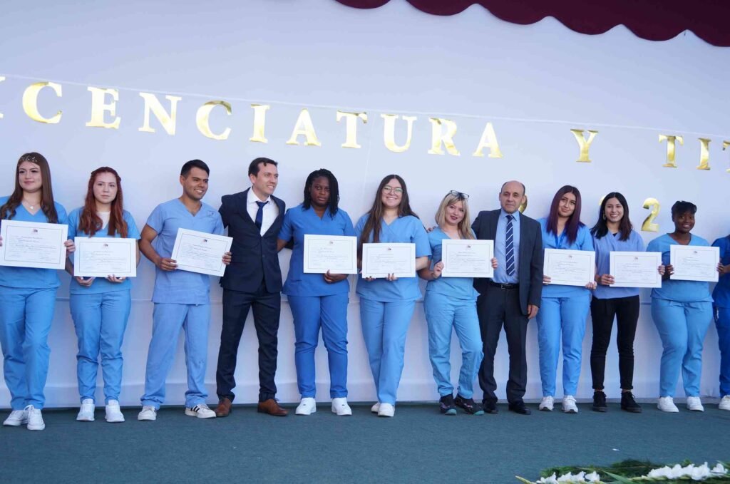 Titulados de Atención de Enfermería con uniforme clínico y su diploma en la ceremonia de Licenciatura